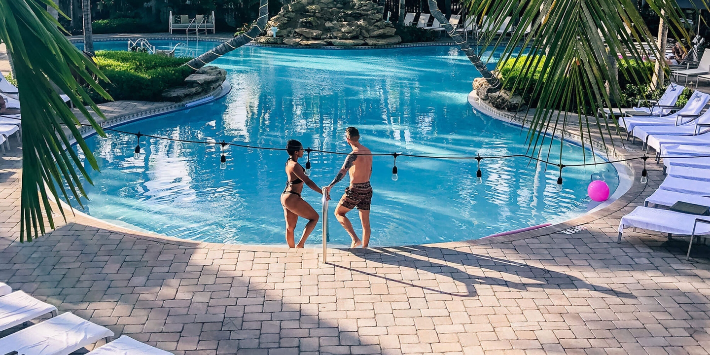A couple pose together at the edge of a resort pool.