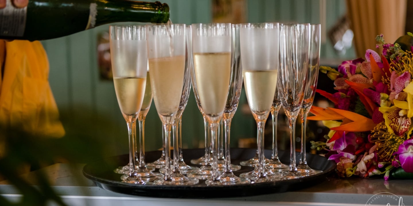 A close up of a hand pouring champagne into flutes set on the tray next to a floral bouquet