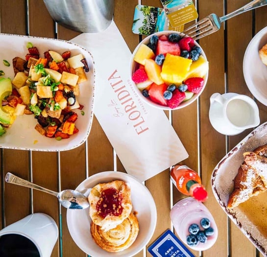 Top down view of a breakfast platter including a fruit bowl, cinnamon buns, and yogurt.