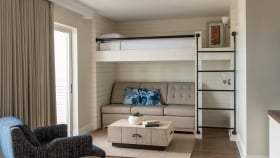 A bunk bed with a black ladder and a couch underneath.